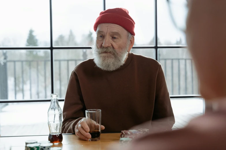 a man sitting at a table with a glass of wine, by Eero Järnefelt, pexels contest winner, hyperrealism, wearing a red backwards cap, nursing home, actor, wearing beanie