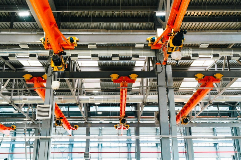 a group of orange robots hanging from the ceiling of a building, pexels contest winner, huge machine cranes, birdseye view, pipelines, 🦩🪐🐞👩🏻🦳