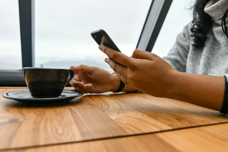 a woman sitting at a table with a cup of coffee and a cell phone, trending on pexels, avatar image, high resolution image, 1 2 9 7, rounded corners