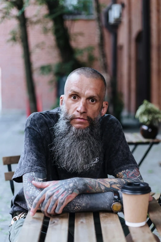 a man sitting at a table with a cup of coffee, a tattoo, unsplash, hyperrealism, he has a beard and graying hair, hairless, aboriginal australian hipster, buzzed hair on temple