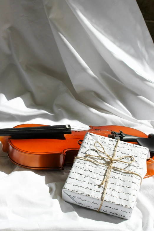 a violin sitting on top of a white sheet, presents, orange and white, holiday season, thumbnail