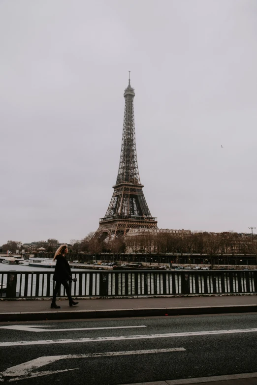 a person walking across a bridge with the eiffel tower in the background, gray skies, 🚿🗝📝, 8 k photo