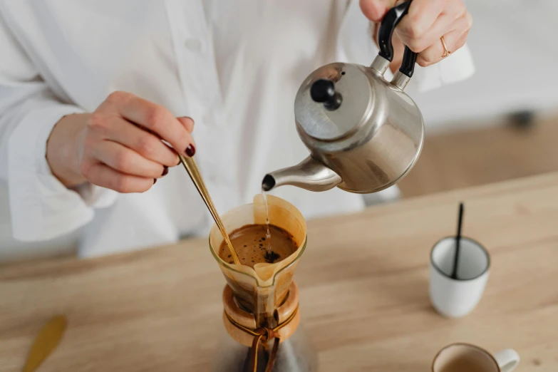 a person pouring coffee into a coffee pot, a still life, trending on pexels, holding a wooden staff, metallic, aussie baristas, thumbnail