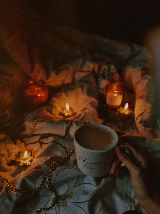 a person sitting on a bed holding a cup of coffee, inspired by Elsa Bleda, pexels contest winner, romanticism, in a room full of candles, ☁🌪🌙👩🏾, ayahuasca ceremony, autumn night