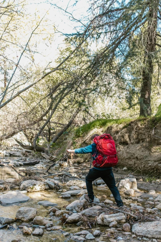 a person with a backpack crossing a stream, malibu canyon, raising an arm, campsites, from waist up