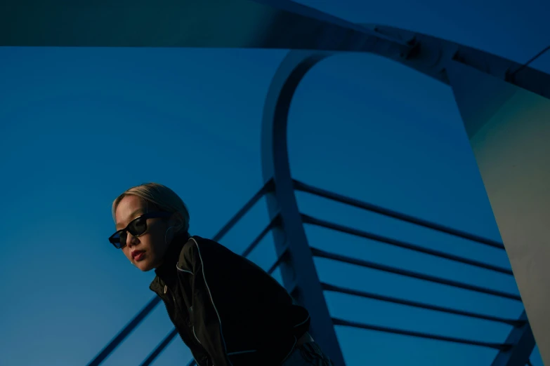 a man riding a skateboard on top of a bridge, an album cover, by Winona Nelson, unsplash, realism, wearing blue sunglasses, portrait of jossi of blackpink, dimly lit, portrait a woman like reol