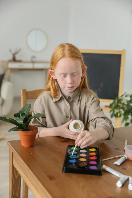 a little girl that is sitting at a table, holding a paintbrush, on a coffee table, plants, red haired teen boy