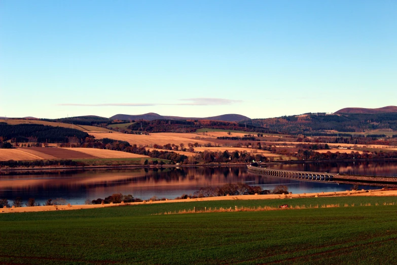 a large body of water sitting next to a lush green field, inspired by John Thomson of Duddingston, pexels contest winner, hurufiyya, autum, bridges, panorama distant view, mies van der rohe