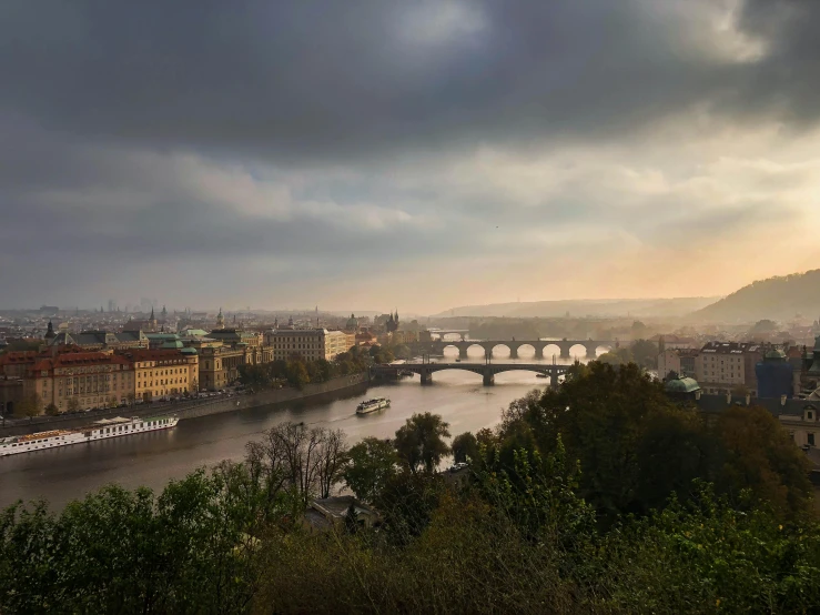 a view of a bridge over a river under a cloudy sky, by Sebastian Spreng, pexels contest winner, art nouveau, prague, panoramic view, slide show, moody hazy lighting