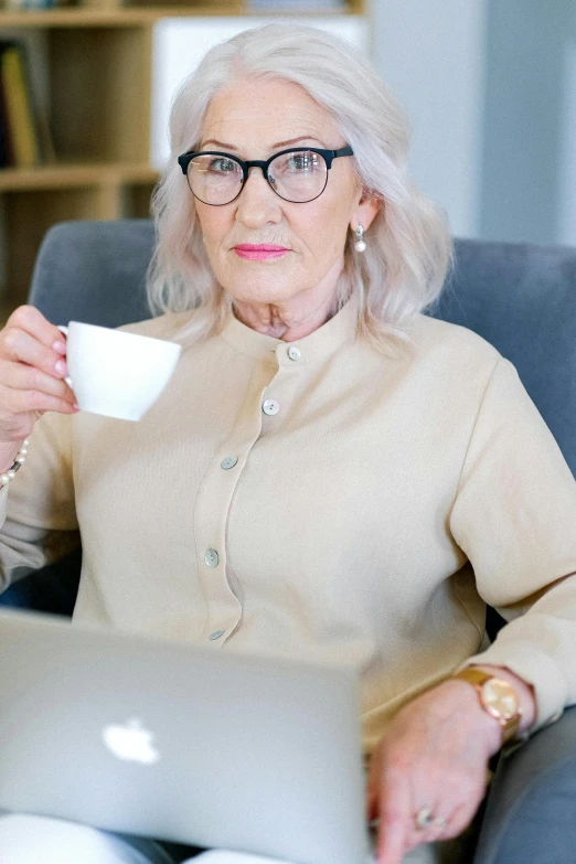 a woman sitting in a chair with a laptop and a cup of coffee, a portrait, by Elaine Hamilton, trending on pexels, elderly woman, square rimmed glasses, annoyed, 15081959 21121991 01012000 4k