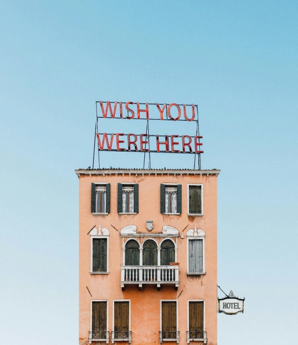 a building with a sign that says wish you were here, a photo, inspired by Wes Anderson, unsplash contest winner, alessio albi, 🚿🗝📝, rooftop romantic, wrought iron architecture