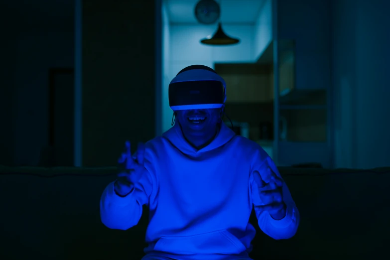 a man sitting on a couch wearing a virtual reality headset, pexels contest winner, holography, moody blue lighting, avatar image, magicavoxel cinematic lighting, excitement