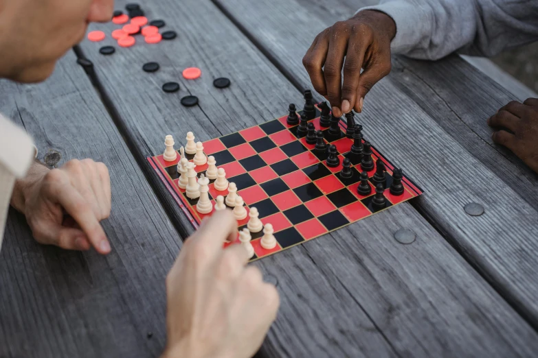 two men playing a game of chess on a picnic table, by Carey Morris, pexels contest winner, back of hand on the table, red and black colour scheme, game pack, black and terracotta