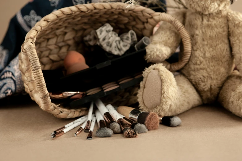 a teddy bear sitting next to a basket filled with makeup brushes, a still life, inspired by artist, earthy colours, beige, brown