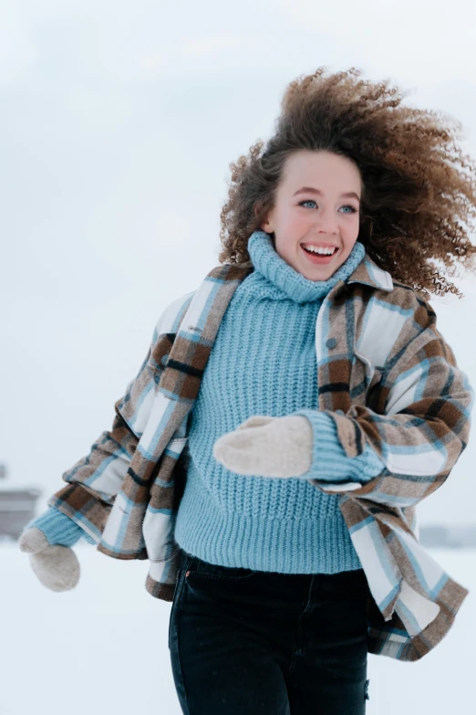 a woman that is standing in the snow, wavy hair spread out, wearing sweater, thumbnail, blue