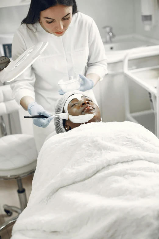 a woman getting a facial treatment in a beauty salon, a digital rendering, trending on pexels, happening, in hospital bed, photo of a black woman, square facial structure, her face is coated in a whitish