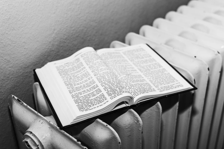 an open book sitting on top of a radiator, a black and white photo, bible, lowres, pelton, realistic »