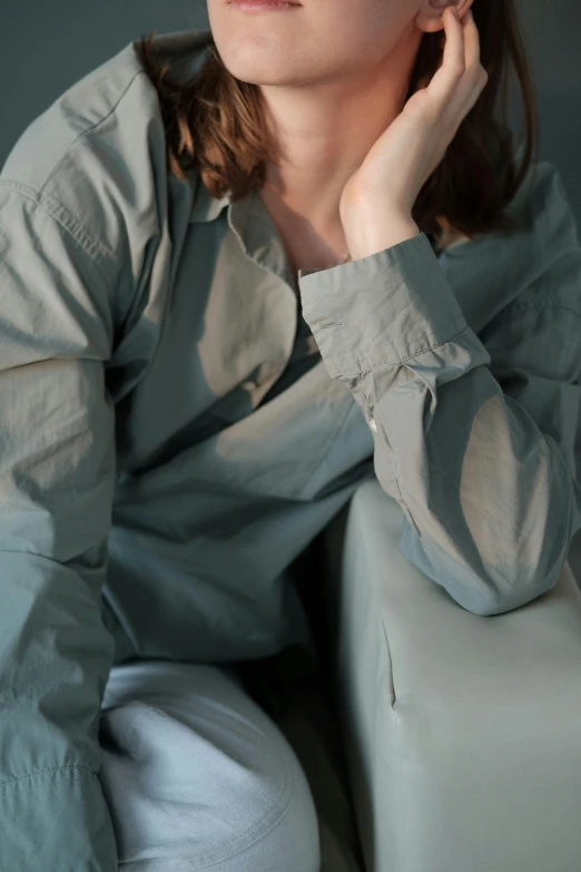 a woman sitting on a couch with her hand on her chin, inspired by Elsa Bleda, trending on unsplash, visual art, pale cyan and grey fabric, green robe, wearing a linen shirt, wearing shirts