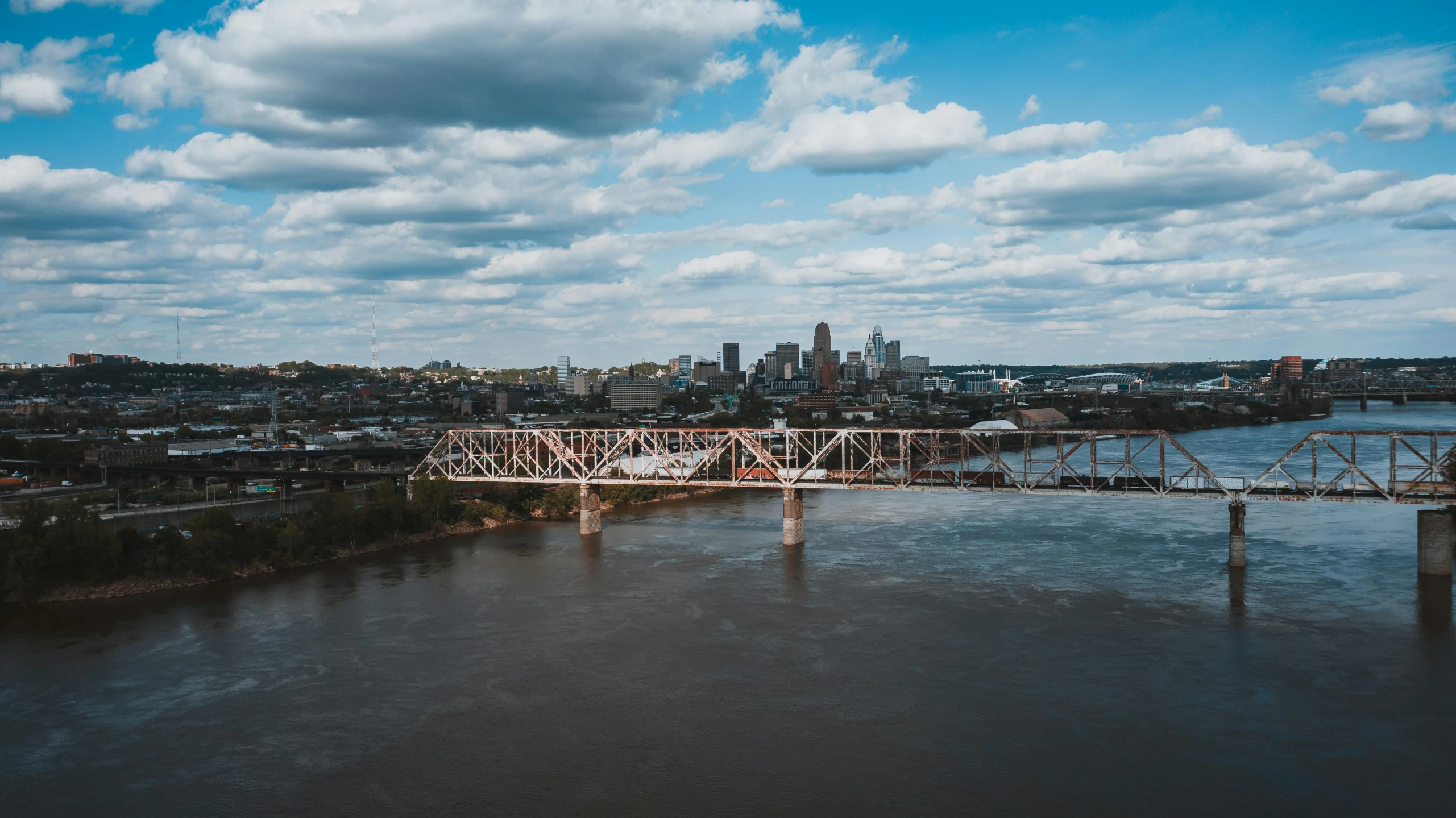 a bridge over a river with a city in the background, by Dan Frazier, pexels contest winner, corporate memphis, wide high angle view, brown, on a bright day