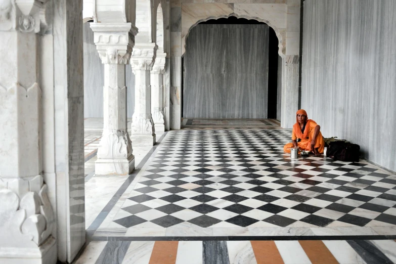 a man sitting on a black and white checkered floor, a marble sculpture, inspired by Steve McCurry, gray and orange colours, inside her temple, white marble interior photograph, islamic