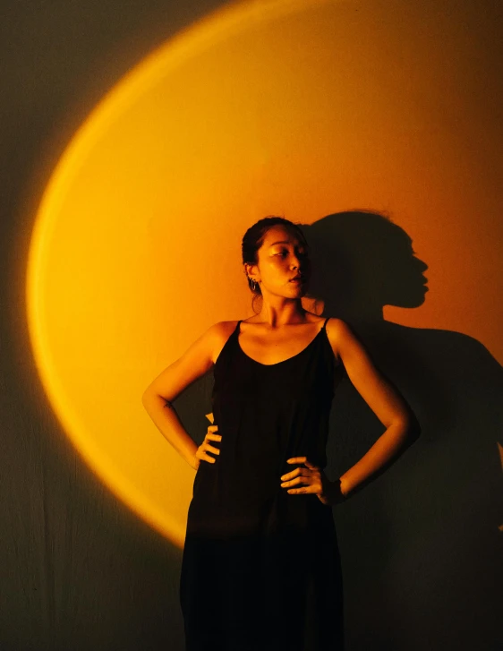 a woman standing in front of a yellow wall, pexels contest winner, light and space, moon backlight, portrait of modern darna, during an eclipse, shadow play