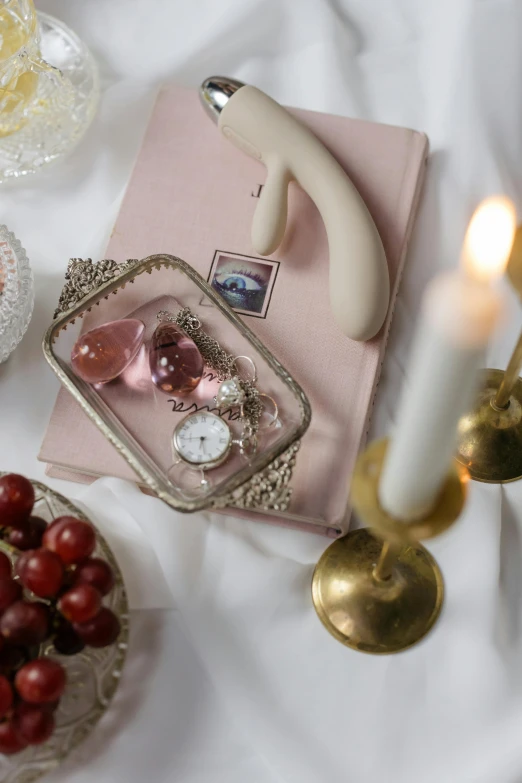 a table topped with a bowl of cherries and candles, inspired by Henriett Seth F., trending on pexels, rococo, books covered in jewels, minimal pink palette, silver，ivory, picture frames