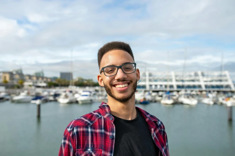 a man standing in front of a body of water, by Washington Allston, pexels contest winner, hurufiyya, smiling slightly, harbour, 21 years old, portrait photo of a backdrop