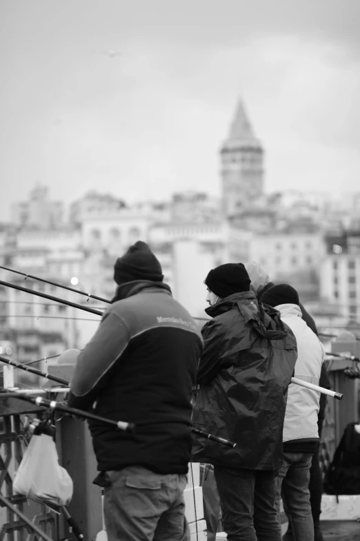 a group of people standing on top of a bridge, a black and white photo, by Tamas Galambos, fish in the background, istanbul, bokeh. i, fishing