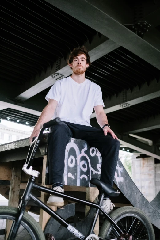 a man sitting on top of a black bike, on a table, connor hibbs, standing on a skateboard, sitting in a chair