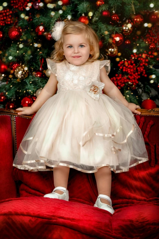 a little girl sitting on a red couch in front of a christmas tree, inspired by Margaret Brundage, baroque, white and gold dress, soft sepia tones, intricate details. front on, wearing a tutu