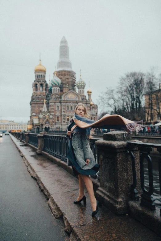 a woman standing on a bridge in front of a church, inspired by Alexander Deyneka, pexels contest winner, baroque, scarf, erin moriarty, russian city, grey