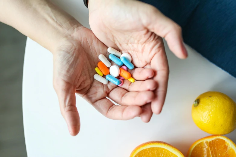 a person holding a bunch of pills in their hands, a still life, by Nicolette Macnamara, pexels, some orange and blue, fruit, where a large, formulae