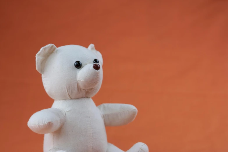 a white teddy bear sitting on top of a table, pexels contest winner, figuration libre, in front of an orange background, children's toy, blank background, 1 5 9 5