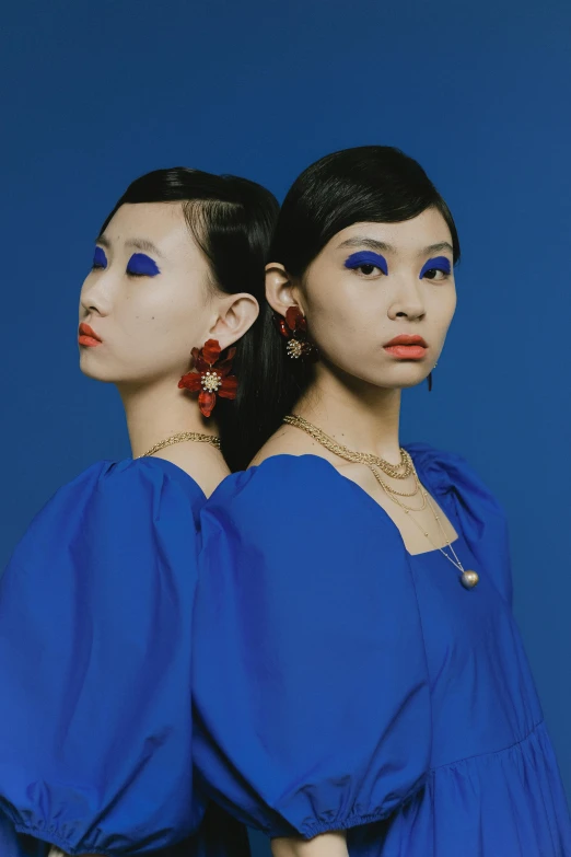 two women in blue dresses standing next to each other, an album cover, inspired by Yves Klein, trending on cg society, cloisonnism, red jewelry, zeen chin and terada katsuya, earring, press shot