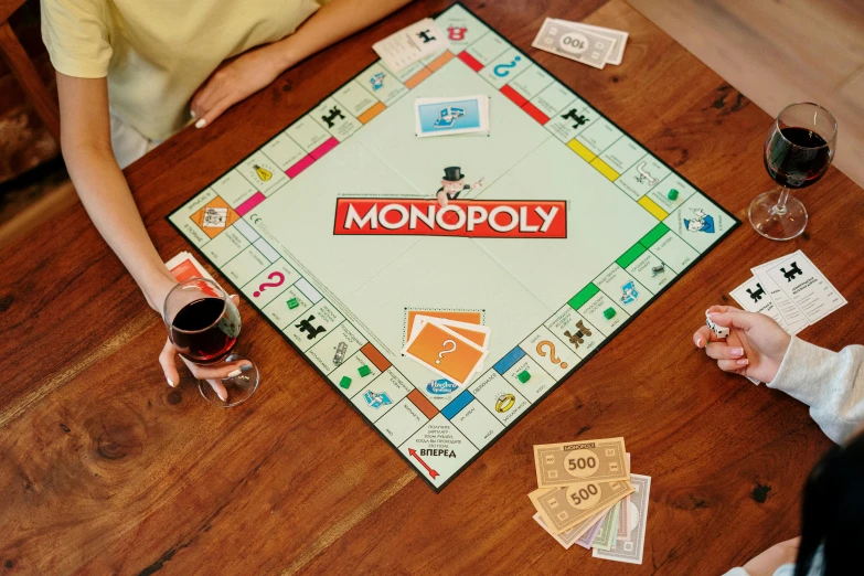 a couple of people sitting at a table playing monopoly, on a wooden table, square, uncrop, 2022 photograph