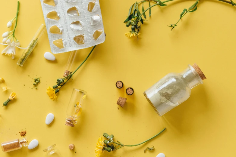a bottle sitting on top of a table next to a bunch of flowers, trending on pexels, plasticien, yellow gemstones, medicine, knolling, dandelion seeds float