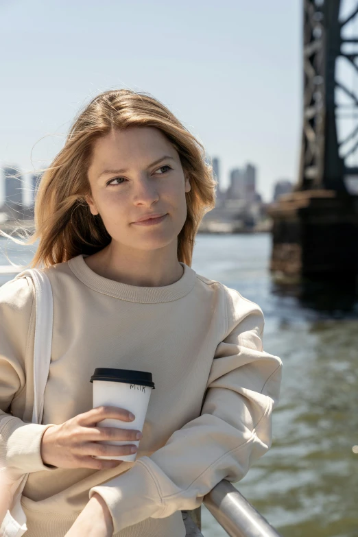 a woman on a boat holding a cup of coffee, inspired by Sydney Carline, happening, wearing sweatshirt, standing in a city street, profile image, promotional image