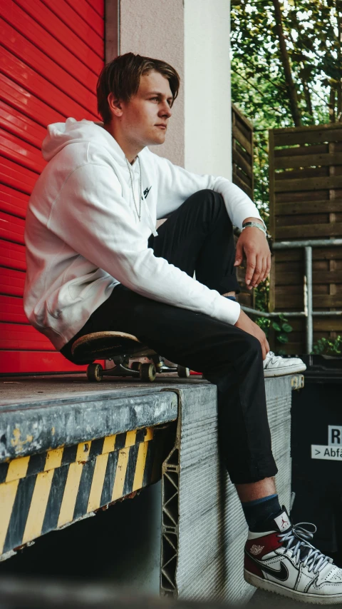 a man sitting on a bench in front of a red building, outlive streetwear collection, 15081959 21121991 01012000 4k, action sports, wearing a white sweater