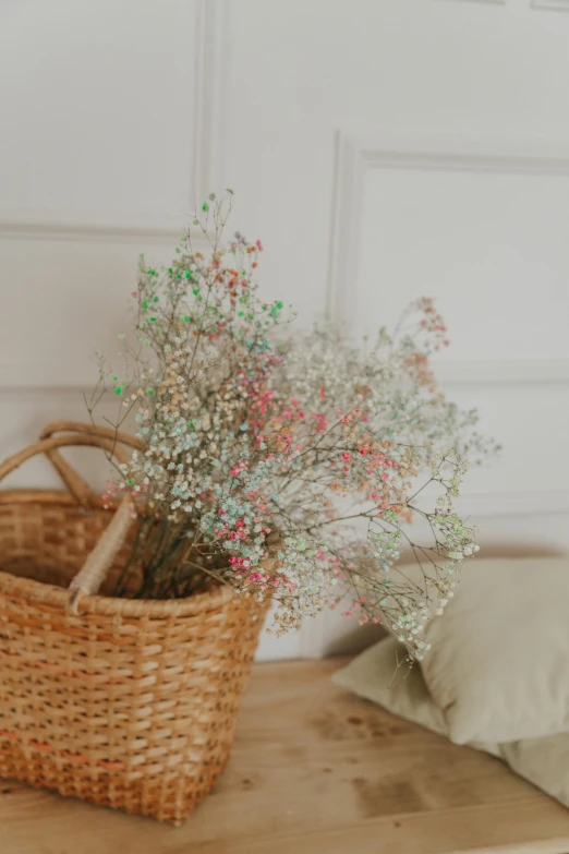 a basket sitting on top of a wooden table next to a pillow, a colorized photo, by Ruth Jên, trending on unsplash, gypsophila, soft bright pastel, made of flowers, detail shot