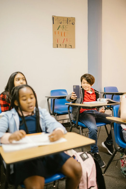 a group of children sitting at desks in a classroom, by Everett Warner, trending on unsplash, ashcan school, calmly conversing 8k, plain background, phone photo, future coder looking on