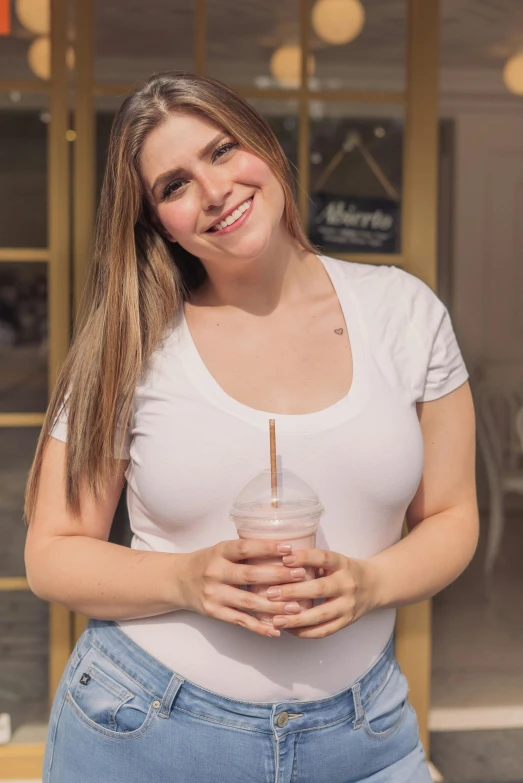a woman standing in front of a building holding a drink, dressed in a white t-shirt, milk and mocha style, plus-sized, kailee mandel