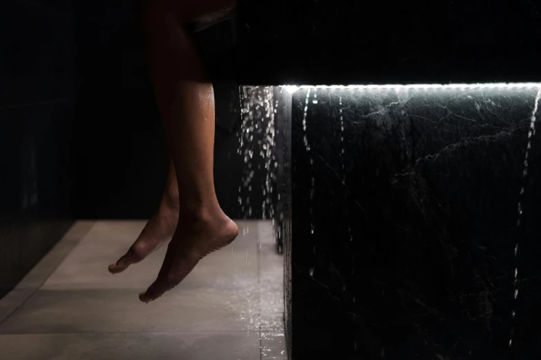 a person standing in front of a waterfall of water, inspired by Peter Zumthor, light and space, accent lighting : : peugot onyx, feet in water, carved black marble, unbeatable quality