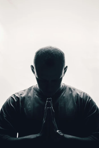 a man in a black shirt is praying, a black and white photo, unsplash, buzz cut, dr dre, character silhouette, dark. no text