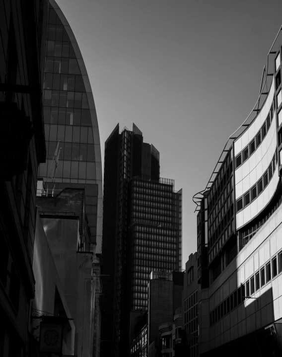 a black and white photo of a city street, inspired by Zaha Hadid, unsplash contest winner, the fabulous city of london, buildings made out of glass, square, evening sunlight