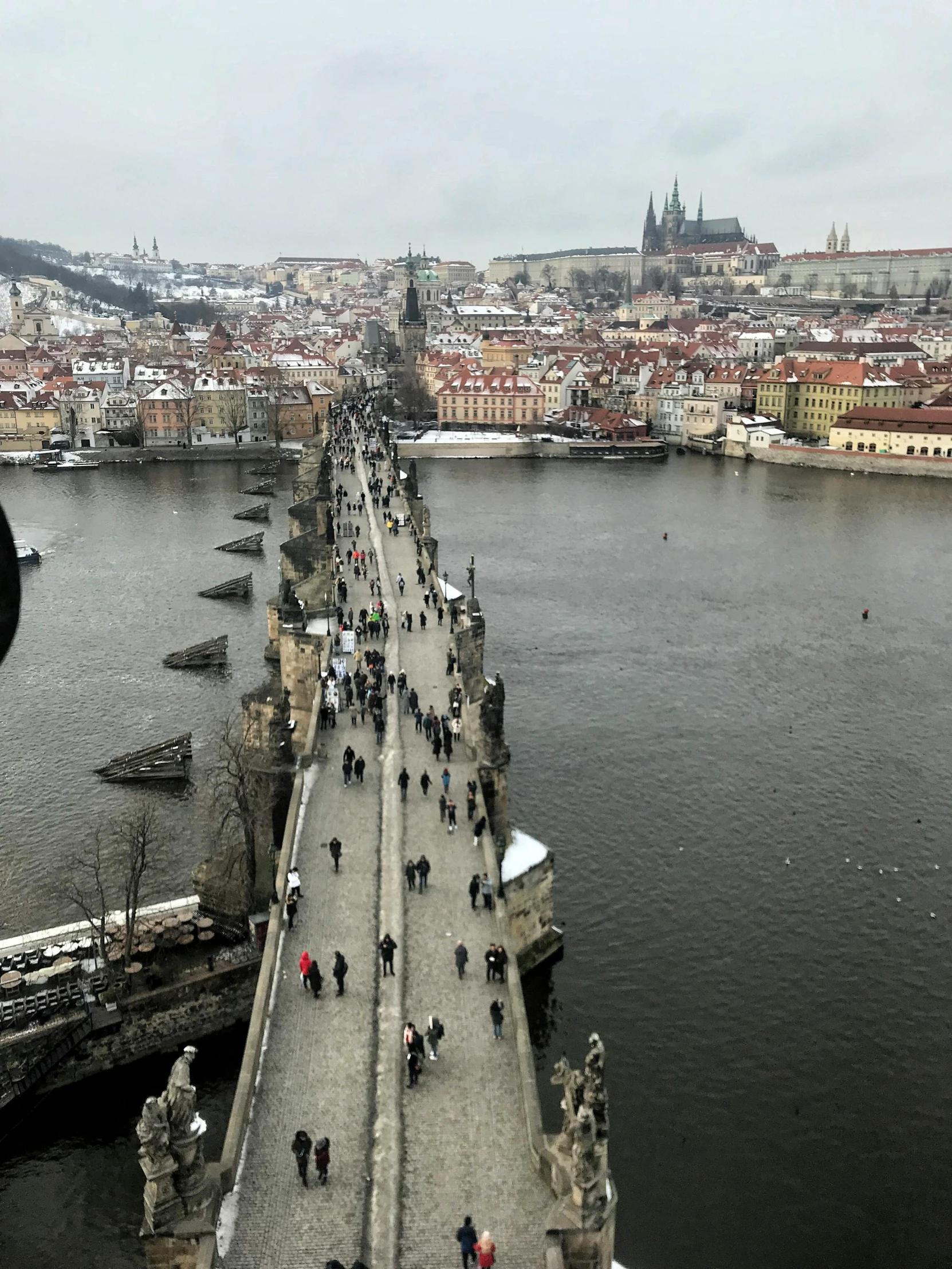 a group of people walking across a bridge over a river, prague in the background, slide show, no filter, looking down on the view