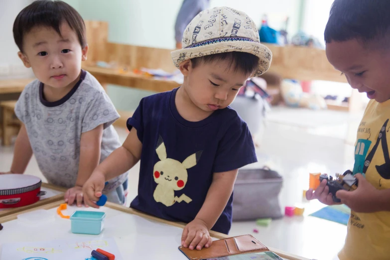 a group of young children standing around a table, inspired by Hikari Shimoda, pexels contest winner, activity play centre, te pae, standing in class, little boy