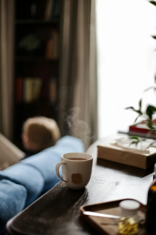 a coffee cup sitting on top of a wooden table, relaxing on a couch, steaming coffee, family friendly, smoke filled room