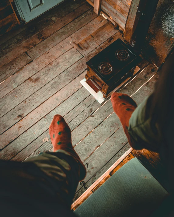 a person standing on a wooden floor next to a stove, inspired by Elsa Bleda, trending on unsplash, in an old west cabin, mid view from below her feet, high view, warm coloured