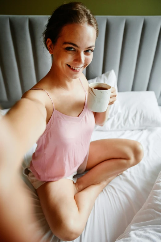 a woman sitting on a bed holding a cup of coffee, happening, taking a selfie, thigh gap, arms open, manuka