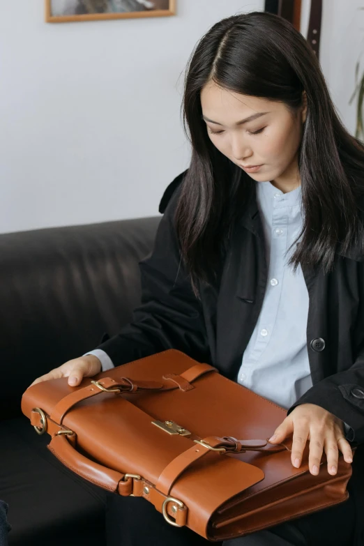 a woman sitting on a couch holding a briefcase, inspired by Ruth Jên, carefully crafted, zoomed in, student, inspect in inventory image